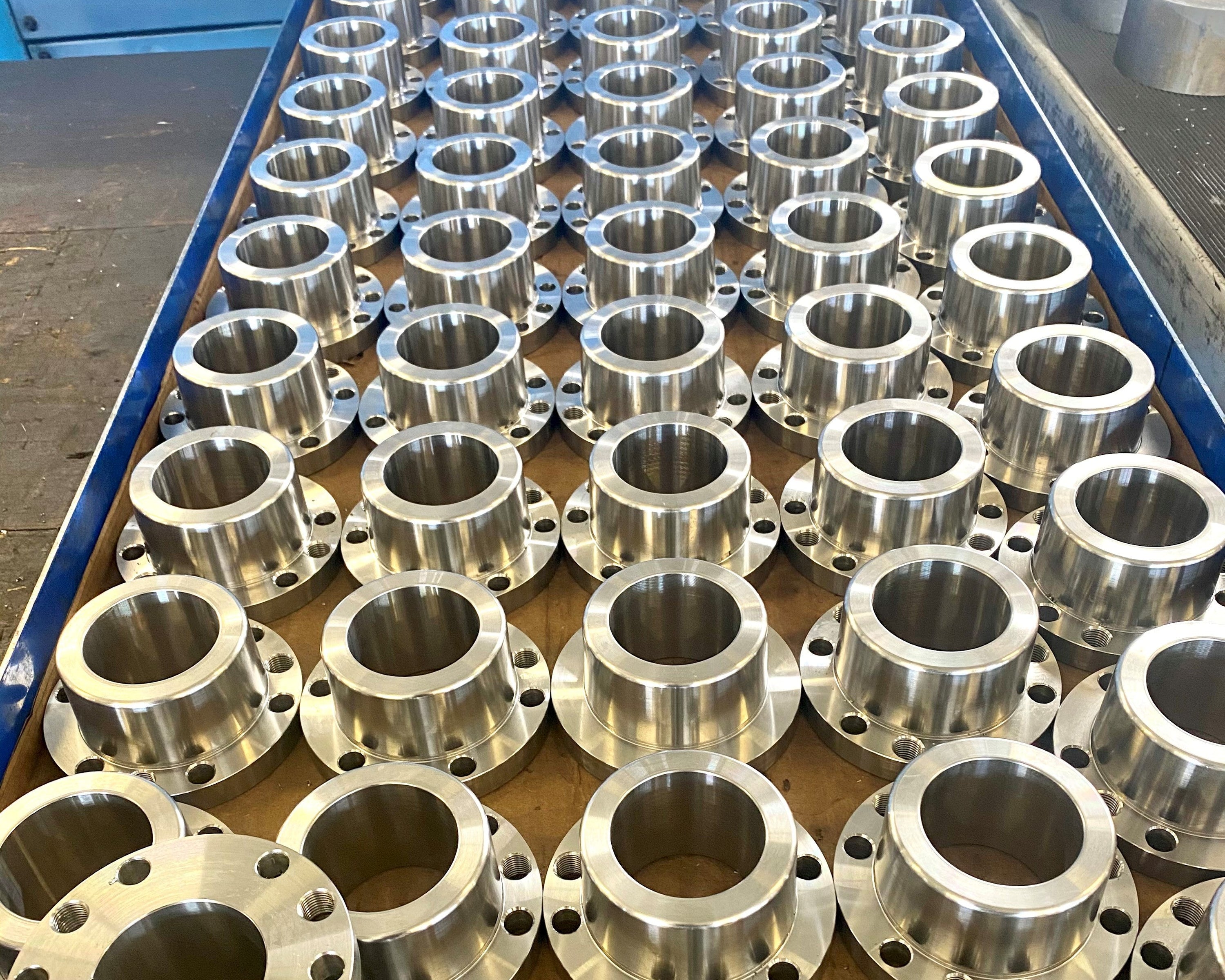 OP Machine and Fabrication Production run of precisioned machined metal flanges arranged on a blue metal tray